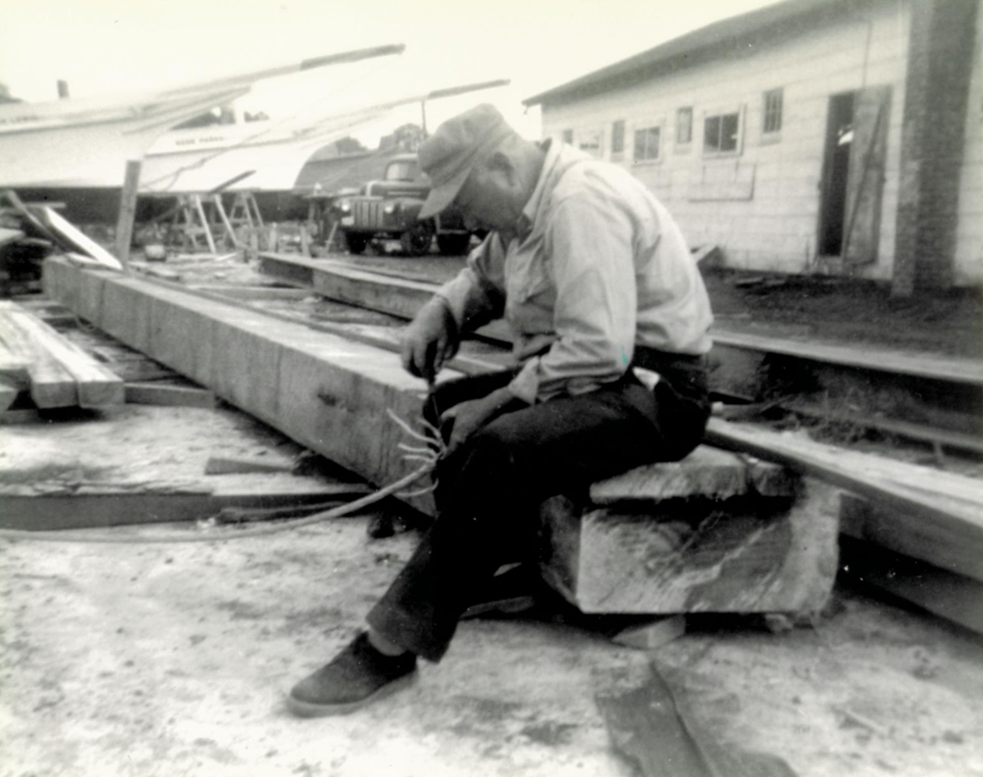 Jim Lewis at Bronza's boatyard. Lewis was the brother of Bronza's wife, Katie, and was Bronza's client for the skipjack Martha Lewis , see in background on the left. Rosie Parks is on the right. Lady Katie is visible, unpainted, in the far background. Undated, probably late 1955, near the completion of the "Three Sisters".