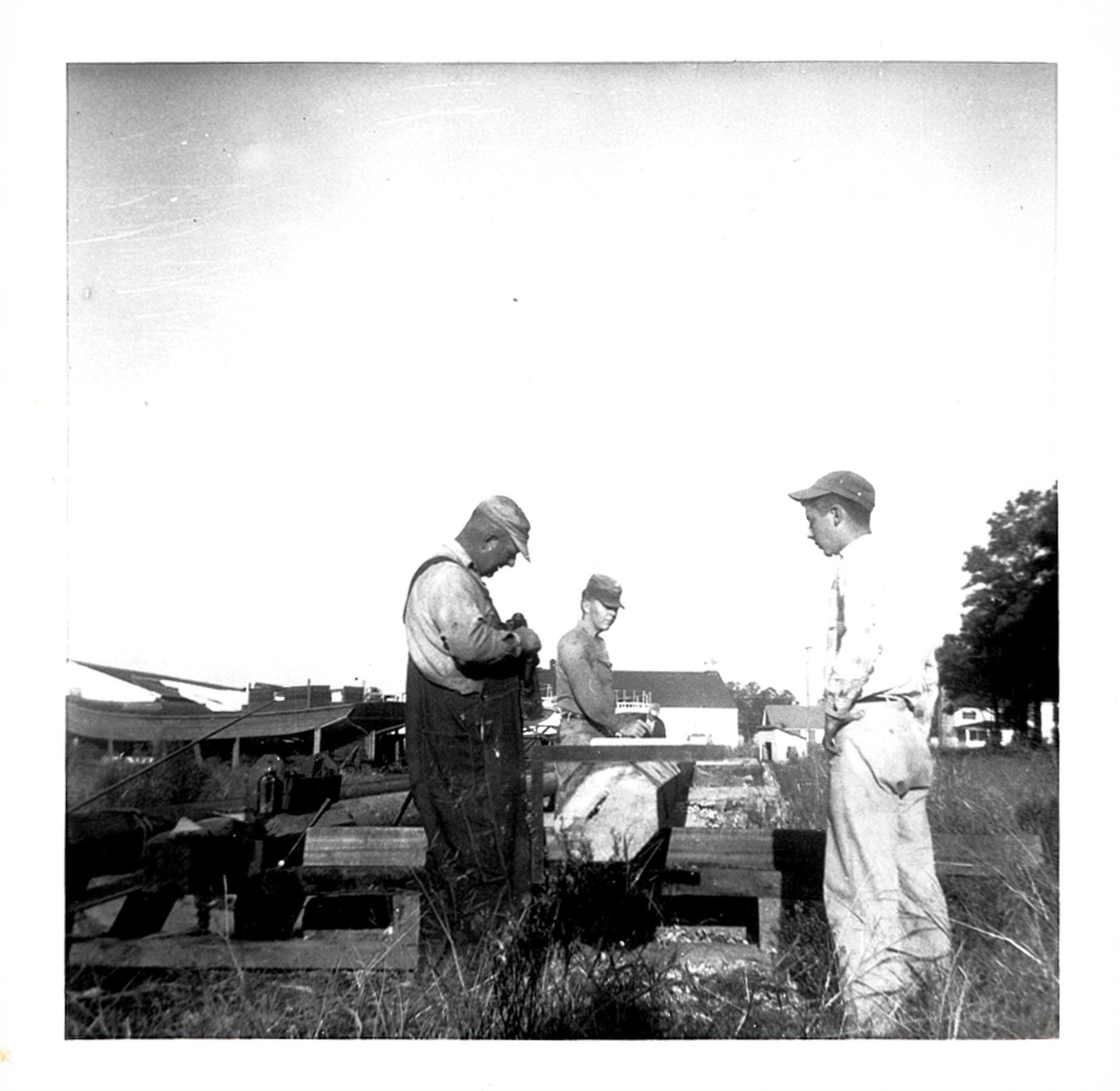 Bronza's crew shaping a mast. Probably the skipjack Lady Katie under construction in the background. October 1955.